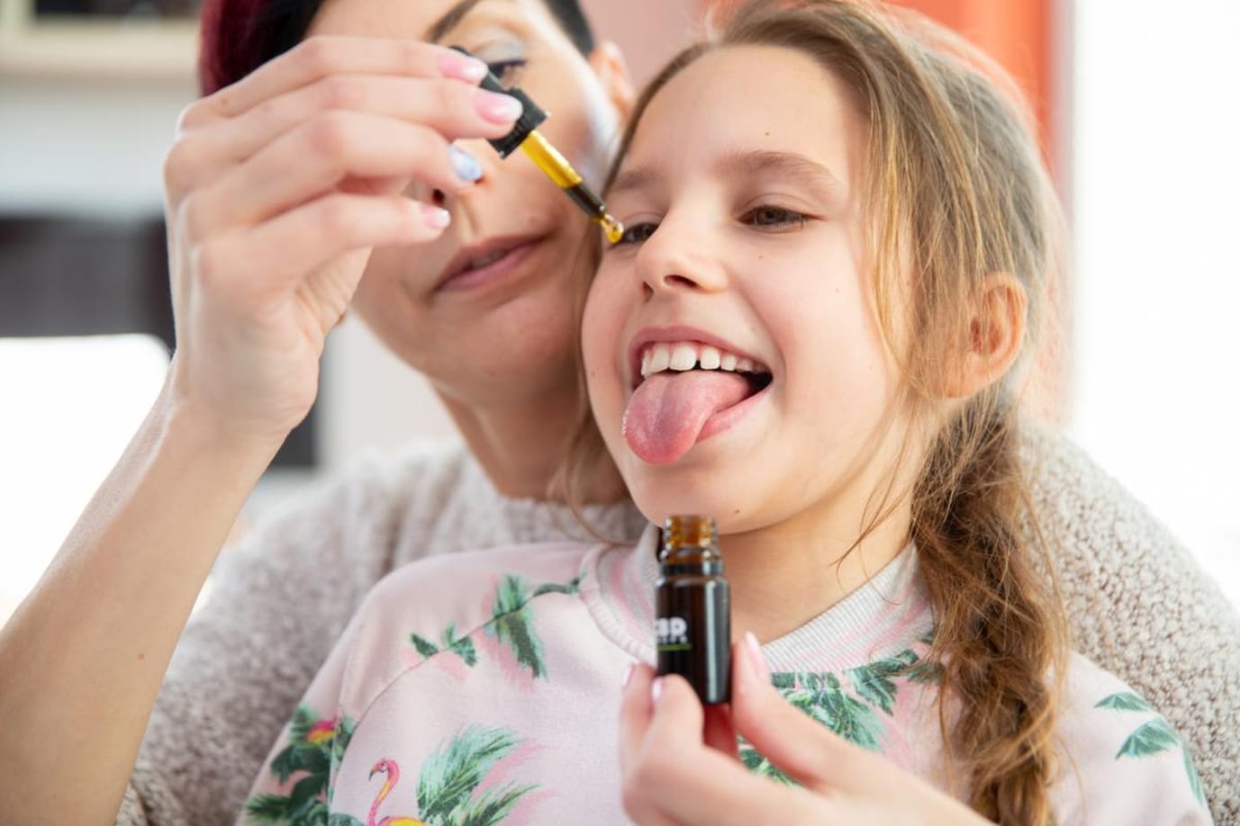 Daughter Sticking Out Tongue To Mother Can Drop CBD Oil Drops on It Foto: Divulgação