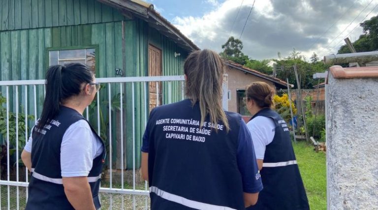 Agentes comunitários de saúde estão em pé na frente de uma casa